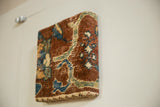 Angled view of the decorative cork board, highlighting the texture and depth of the antique rug fragment.