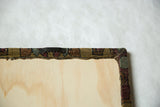 Sawtooth wall hanger on the wood back of a cork board framed with an antique rug fragment.