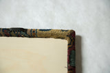 Back corner of the decorative cork board showing the sawtooth hanger and wrapped Kerman rug edge.