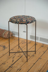 Reclaimed side table with an antique rug fragment top on its slender metal folding base.