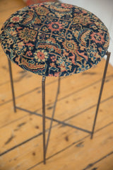 Reclaimed side table featuring a round, cushioned top made from an antique Persian rug fragment.