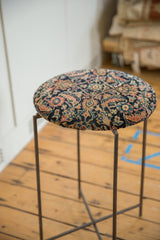 Angled perspective of a side table with a cushioned top made from an antique Persian rug fragment.