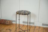 Reclaimed side table featuring a cushioned antique rug top on a slender vintage metal frame.