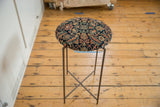 Side table featuring a patterned antique rug top and a slender, dark metal folding base.