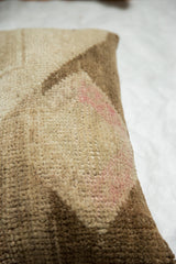 Textured, distressed beige Oushak rug fragment pillow with faded pink.