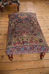 Antique Kerman rug ottoman from a three-quarter angle showing the floral textile and curved wooden legs.