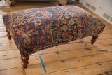 Antique Kerman rug ottoman showing its upholstered profile and curved wooden legs.