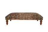 Antique Persian Kerman rug ottoman featuring a floral pattern in red, blue, and ivory on turned wooden legs.