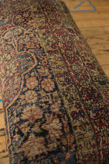 Angled perspective on the antique Kerman ottoman's richly textured rug fragment upholstery.