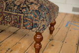Corner detail of an antique rug ottoman showing the Kerman textile weave and turned wood leg.