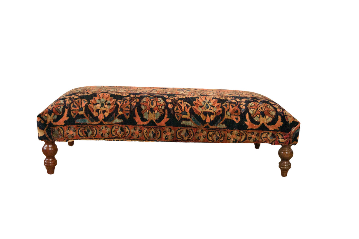Vintage Persian rug ottoman with floral terracotta and jade green patterns on dark turned wood legs.