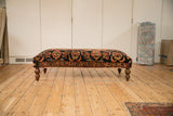 Long profile of a vintage Persian rug ottoman with intricate floral upholstery on turned wood legs.