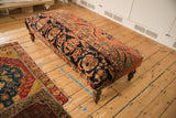 Vintage Persian rug ottoman showing its full length, patterned top, and dark turned legs.