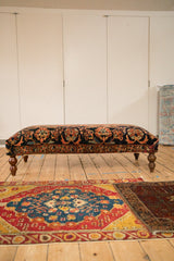A long vintage Persian rug ottoman coffee table shown in full profile on turned wooden legs.