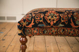 A vintage Persian rug ottoman's corner, showing the traditional pattern and curved wooden leg.