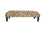 Reclaimed Moroccan rug ottoman with an abstract geometric design in ivory and dark gray on dark turned legs.