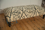 Vintage Moroccan rug ottoman showing the plush, textured geometric surface and dark curved leg.