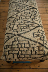 Shaggy, high-pile texture of the Moroccan rug ottoman's abstract gray and ivory design.