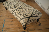 Angled view of the long vintage rug ottoman showing its plush geometric texture and dark wooden leg.