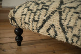 Plush texture of a Moroccan rug ottoman corner with a dark, turned wooden leg.