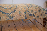 Textured side of a vintage rug ottoman with blue floral patterns and a dark turned leg.