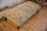 Long vintage Persian rug ottoman with gold, ivory, and blue motifs on turned wooden legs.