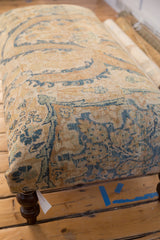 Detail of a vintage rug ottoman's corner with textured Persian upholstery and a dark curved leg.