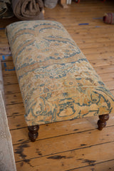 A long ottoman upholstered in vintage Persian rug with blue and gold motifs on dark turned legs.