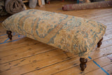 Close-up of the vintage Persian rug ottoman's dark, turned wood leg and side upholstery.
