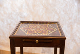 Dark wood table top with Matt Ulrich's red, gold, white geometric dot painting.
