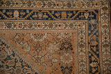 Close-up of the vintage Malayer rug corner showing its navy vine border and worn copper field.