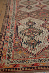 Intricate geometric border and shield medallion with soft camel, coral, ivory tones.