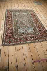 Distressed Kurd rug corner showing madder root rust geometric border with meandering vine and fringe.
