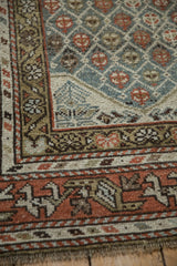 Distressed Kurd rug detail: geometric meandering vine border, lattice field, slate blue, rust tones.