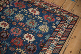 Corner of an antique Caucasian rug with serrated floral motifs and a complex, rainbow-shaded border.
