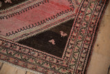 Corner of a distressed Malayer rug showing blush bird motifs in a chocolate brown spandrel.