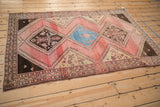 Angled view of a vintage Malayer rug showing its geometric diamond medallions and striated pink field.