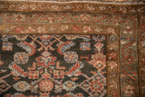 Distressed Hamadan rug corner, charcoal Herati motif with red, blue, and multi-toned brown borders.