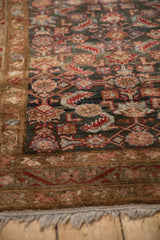 Distressed vintage Hamadan rug corner with Herati pattern, showing charcoal, ruby, and coffee tones.