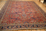 Angled view of a vintage Heriz rug with scrolled navy vines across its cherry red floral field.