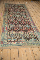 Angled view of a vintage Persian runner with repeating botehs on a chocolate brown field.