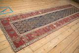 Angled view of an antique Persian rug runner's navy boteh field and vibrant red geometric border.