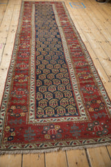 The long profile of an antique Persian runner, showing the navy boteh field and red floral border.
