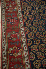 Detailed view of the navy blue boteh field and red floral border of an antique Persian rug.