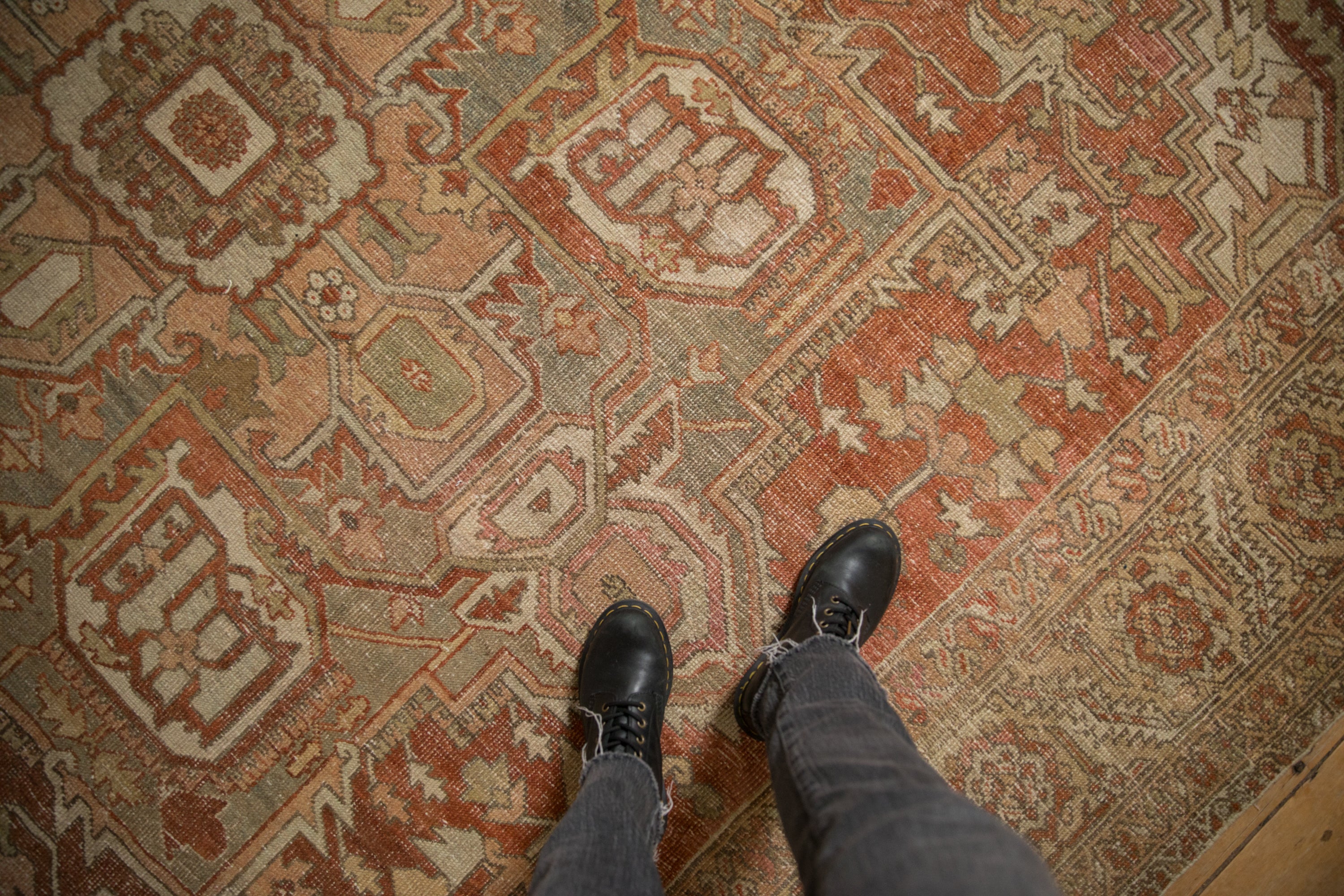 Worn, low-pile texture of a vintage Heriz carpet showing its geometric design in dusty red, sage, and platinum.