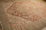Angled view of a distressed Heriz rug's worn texture over geometric patterns in dusty red and sage.