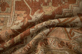 Textural folds in a distressed Heriz rug showing visible knot heads and soft brick red tones.
