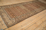 Vintage distressed Hamadan runner with a brown boteh pattern, viewed from a low angle down its length.