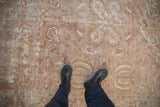 The worn, low-pile texture of a distressed Sultanabad carpet with faded botanical designs.