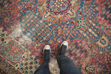 Intricate red and blue floral field of an antique Kerman rug, with visible pile wear.